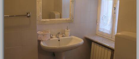 Un baño con lavamanos pedestal, inodoro, bidé y espejo con luz.