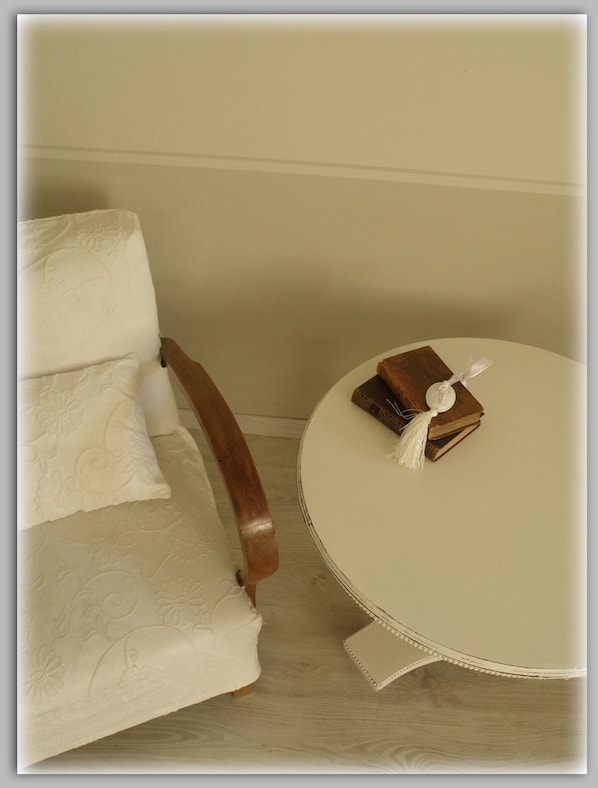 A chair with a wooden armrest and a round table with a book and a white object on it. - Cascina Luvot (Melazzo)