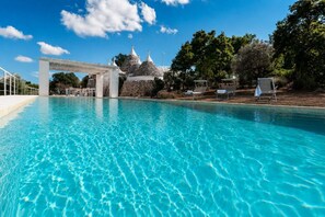 A swimming pool with clear water, a white gazebo, and stone structures in the background.