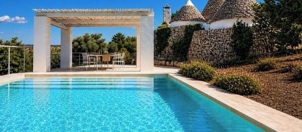 A swimming pool with a pergola and seating area, surrounded by stone walls and greenery.