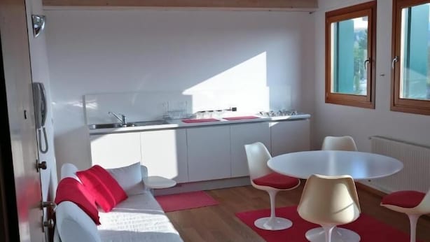 A modern kitchen with a built-in stove and a dining area with a white table and red chairs. - Oleaclub Locazione Turistica (Maser)
