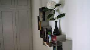 A corner with a grey wardrobe, a black vase with a white flower, and a black shelf with books and a magazine. - Oleaclub Locazione Turistica (Maser)
