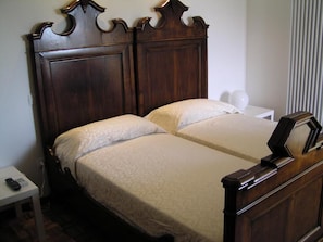 A double bed with a wooden headboard, a bedside table with a lamp, and a window with vertical blinds. - Oleaclub Locazione Turistica (Maser)