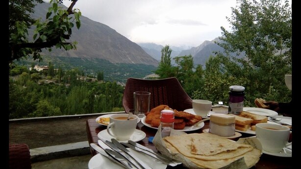 A table set for breakfast with a mountain view, including plates of food, cups, and cutlery. - Baltit Heritage Inn (Karimabad)