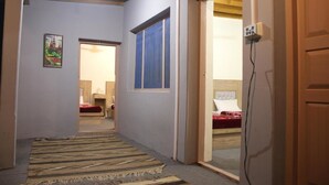 A hallway with a striped rug, a door leading to a bedroom with a bed, and a wall-mounted power outlet. - Baltit Heritage Inn (Karimabad)