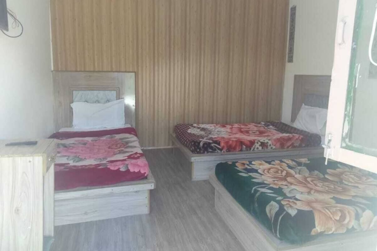A bedroom with two beds, each with a floral bedspread. The room has a wooden headboard and a wooden floor.