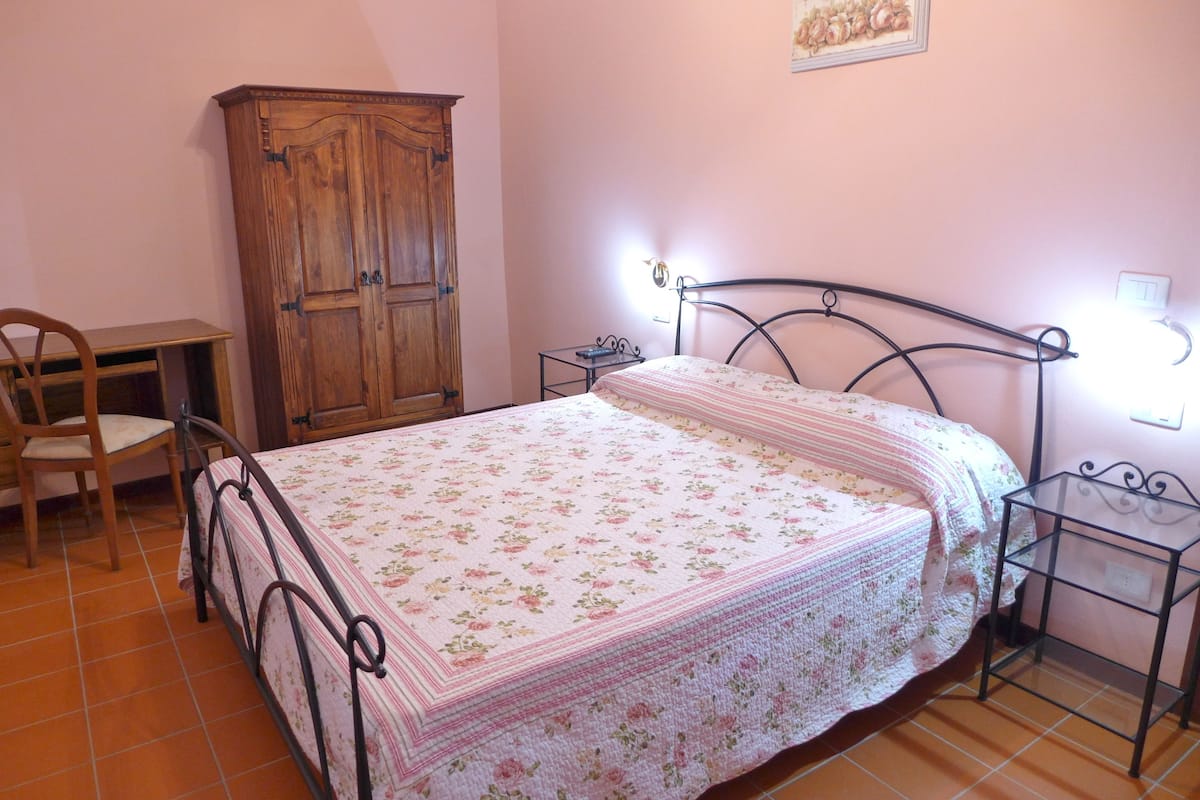 A bedroom with a bed, a wooden wardrobe, a desk, and a chair.