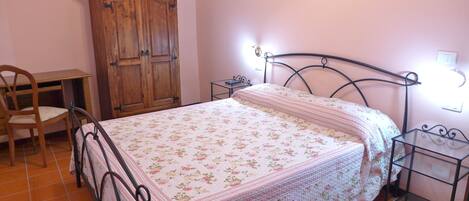 A bedroom with a bed, a wooden wardrobe, a desk, and a chair.