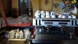A coffee machine with cups and saucers, a basket, and a shelf with bottles. - Hotel Paese Corvara (Beverino)