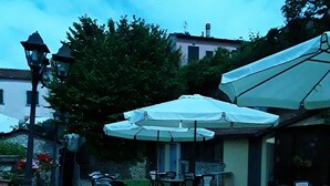 An outdoor seating area with tables and chairs, umbrellas, and a lamp post. - Hotel Paese Corvara (Beverino)