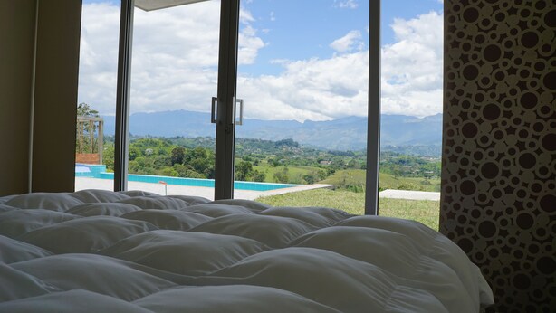 Un dormitorio con una cama grande, vistas a una piscina y montañas al fondo.