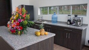 Una cocina con encimeras de granito, armarios de madera oscura, dispensador de agua, cafetera y ventana con vista a un jardín.