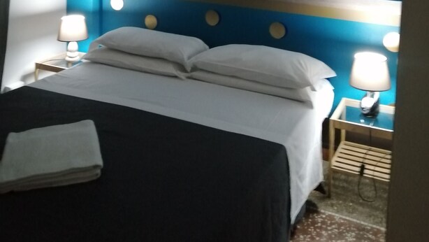 Ein Hotelzimmer mit einem Bett, zwei Nachttischlampen, einem Nachttisch und einer Wand mit blauem Muster.