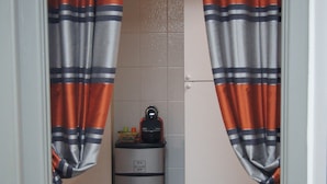 Eine schmale Küche mit Kühlschrank, Mülleimer und einer kleinen Arbeitsfläche mit Wasserkocher.