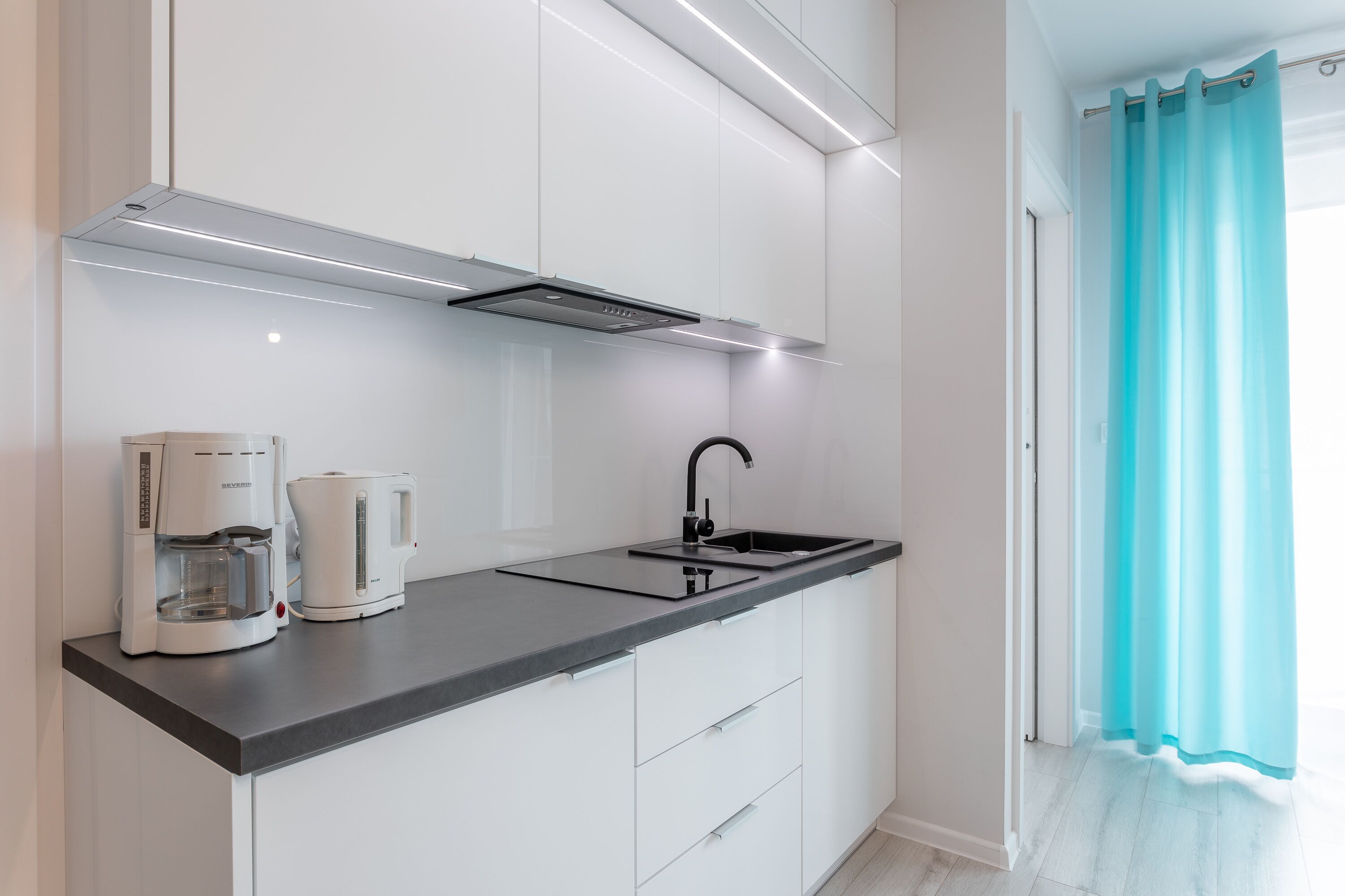 A modern kitchen with white cabinets, a black countertop, a coffee maker, and a sink.