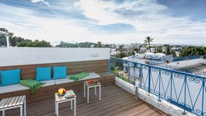 A rooftop terrace with a wooden deck, seating area with cushions, and a table with food and drink. - Appartement Les Musiciens (Sidi Bou Said)