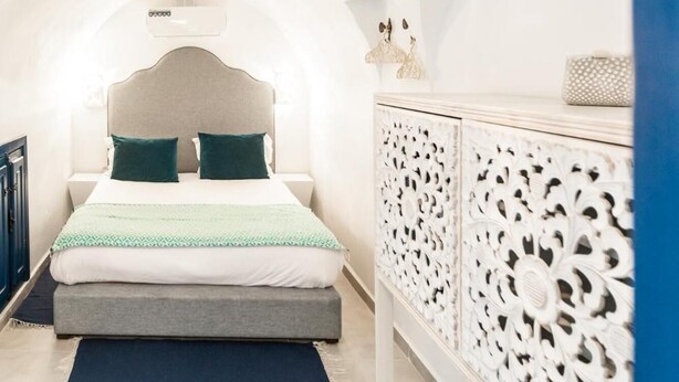 A bedroom with a bed, a nightstand, a dresser, and a decorative wall panel. - Appartement Les Musiciens (Sidi Bou Said)