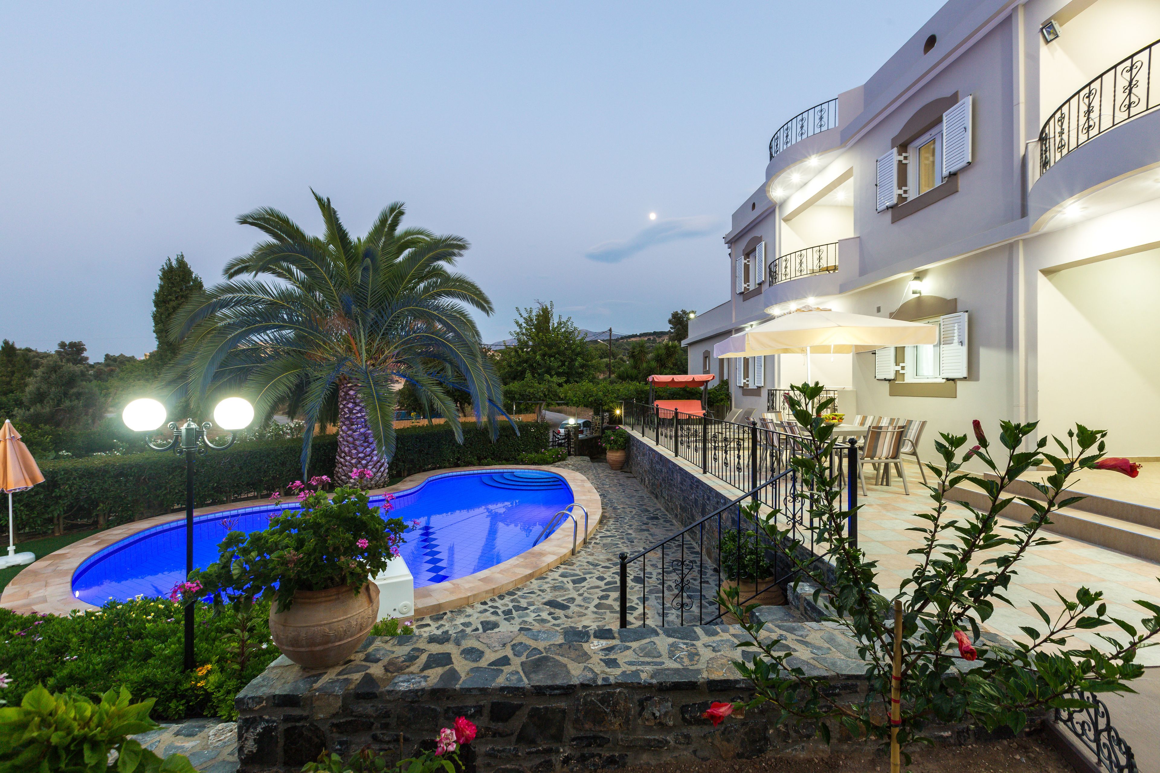A pool area with a stone deck, palm trees, and a building with balconies and outdoor seating.