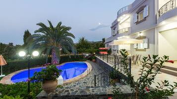 A pool area with a stone deck, palm trees, and a building with balconies and outdoor seating.