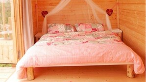 A wooden cabin bedroom with a canopy bed, a small table, and a red mat on the floor. - Bleckmanns Hof (Werne)