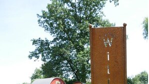 A rustic wooden sign with the name "Wilkomen" in a rural setting with a red barn and wooden structures in the background. - Bleckmanns Hof (Werne)
