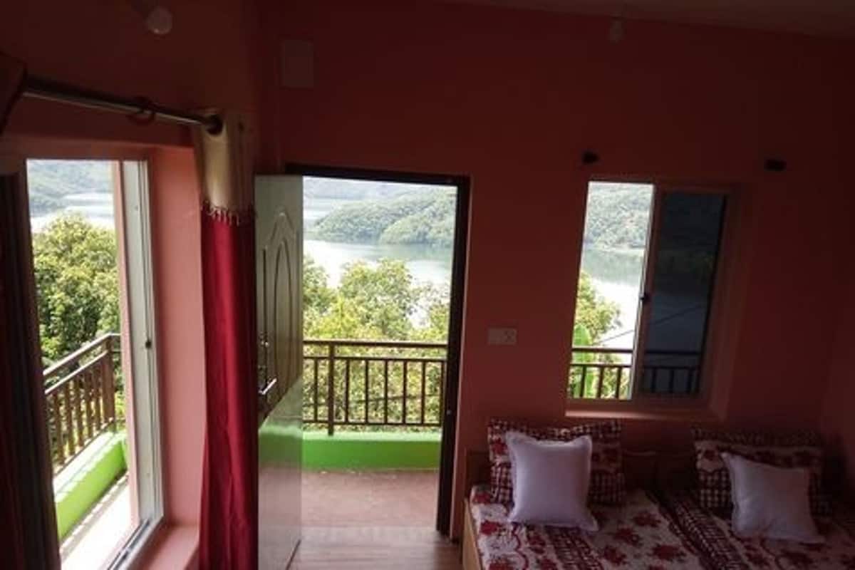 A room with a bed, a window with a view of greenery, and a balcony with a railing.