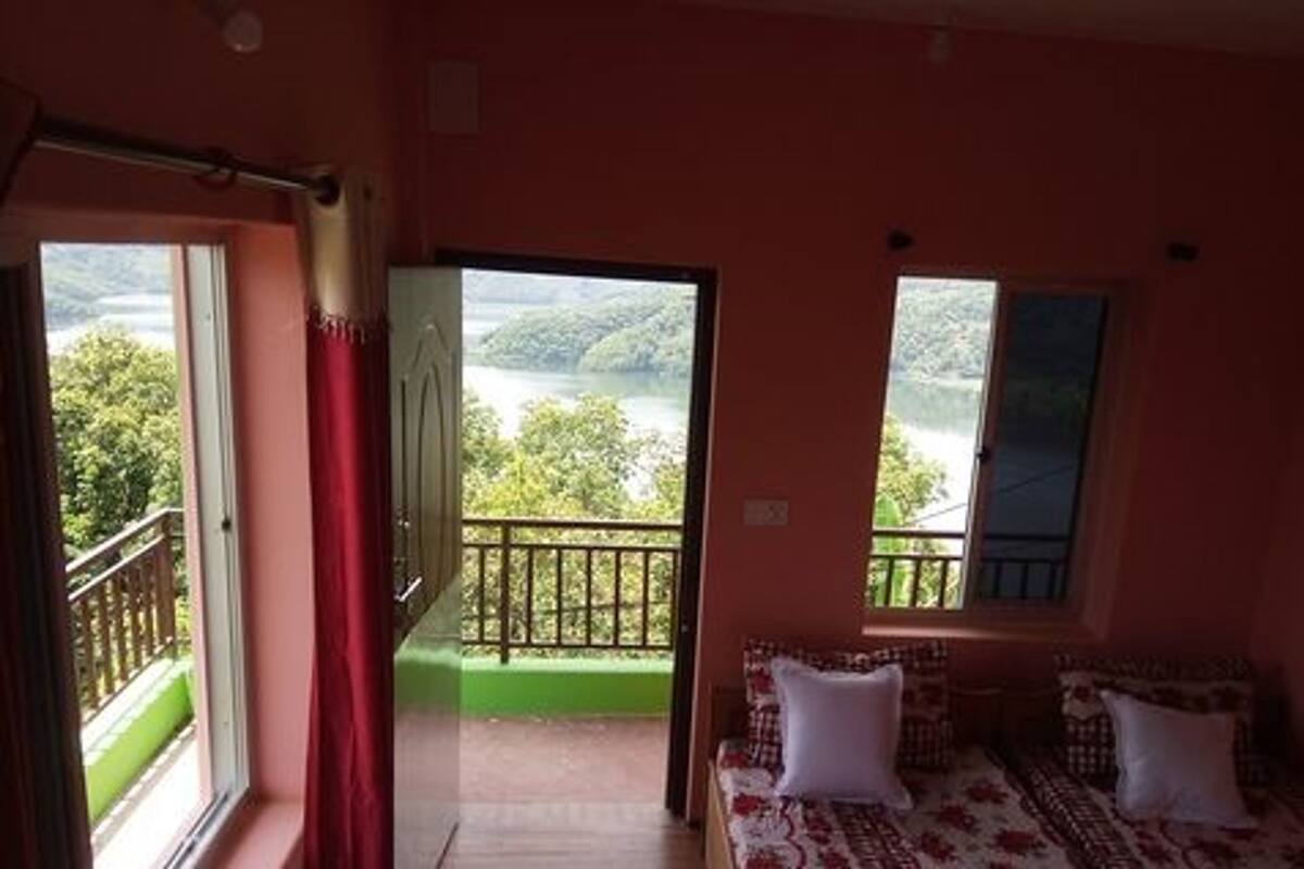 A room with a bed, a window with a view of greenery, and a balcony with a railing.