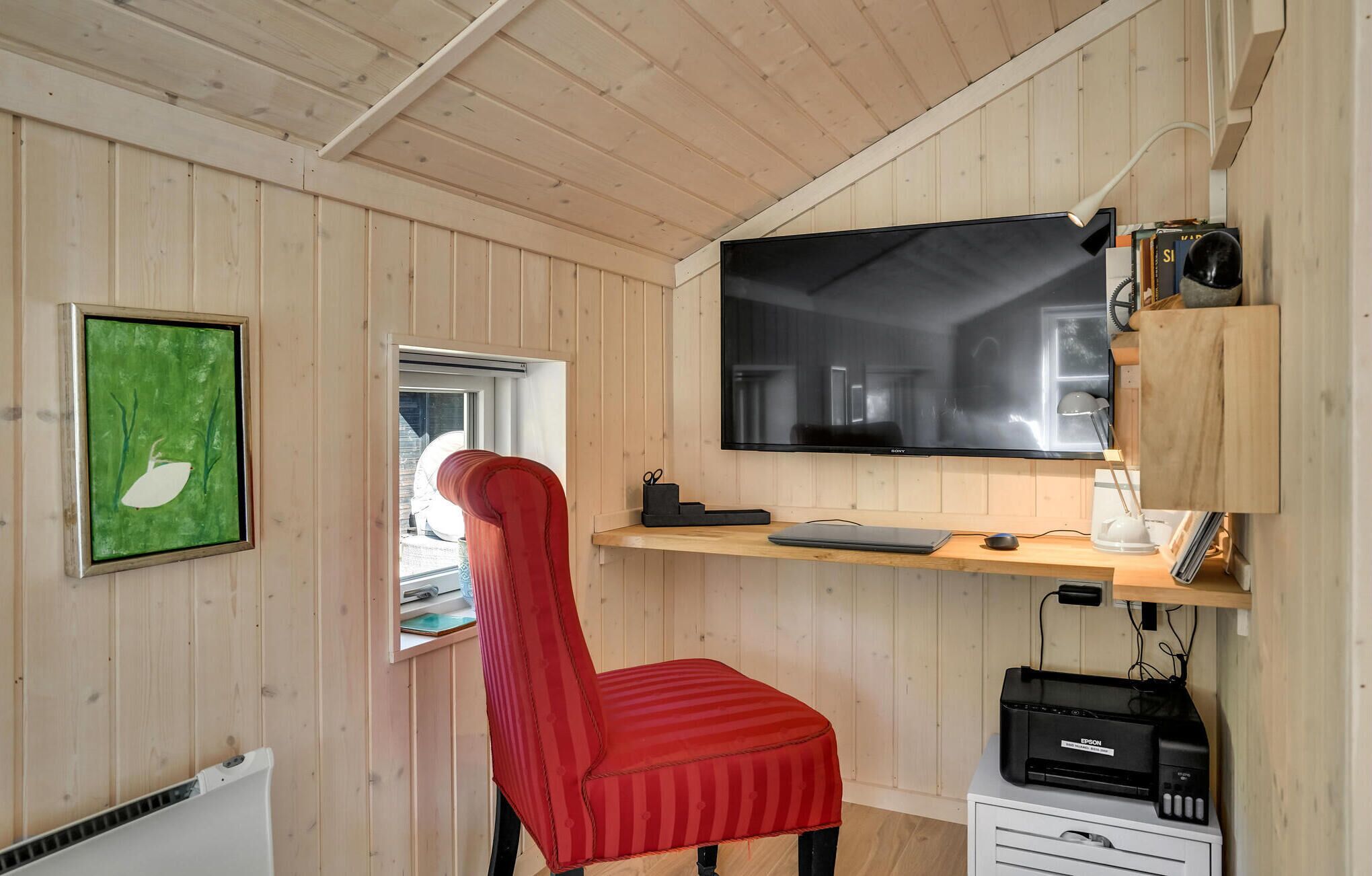 Une pièce avec un intérieur en bois, une chaise rouge, un téléviseur fixé sur une étagère en bois et une fenêtre.