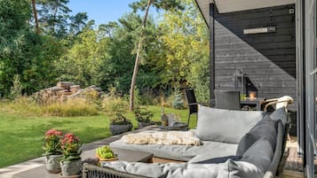 Un espace de détente extérieur accueillant, avec un canapé, des fauteuils et une table, entouré d’une végétation luxuriante et d’un bâtiment en bois.