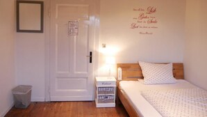 Un dormitorio con puerta de madera, una mesita de noche con lámpara, una cama con colcha estampada y un adorno de pared con texto.