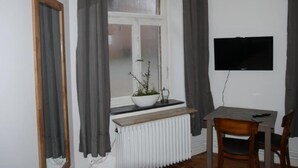 Una habitación con ventana, radiador, mesa, silla y televisor montado en la pared.