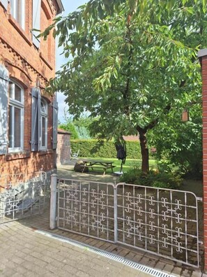 A brick building with a metal gate, a tree, and a bench in a courtyard. - Gästehaus Alte Schmiede (Ascheberg)