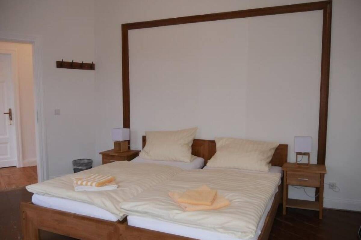 A double bed with wooden headboard and footboard, two bedside tables with lamps, and a small shelf on the wall.