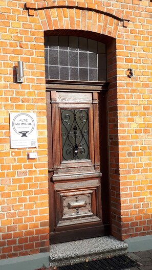A brick building with a wooden door and a metal gate. A sign on the wall reads "ALTE SCHMIEDE GASTEAUS 1904". - Gästehaus Alte Schmiede (Ascheberg)