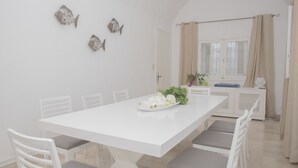 Un comedor con una mesa y sillas blancas, una planta pequeña en la mesa y peces decorativos en la pared.