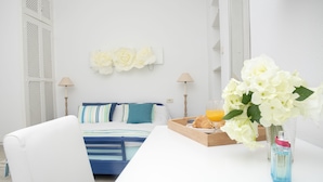 Un dormitorio con cama, lámparas de noche, mesita de noche con una bandeja de desayuno y un jarrón de flores.