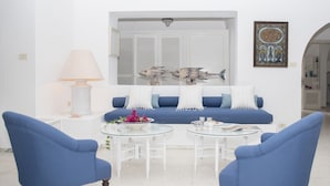 Una sala de estar con un sofá, dos sillones azules, una mesa de centro de vidrio, una lámpara blanca y una escultura decorativa de un pez.