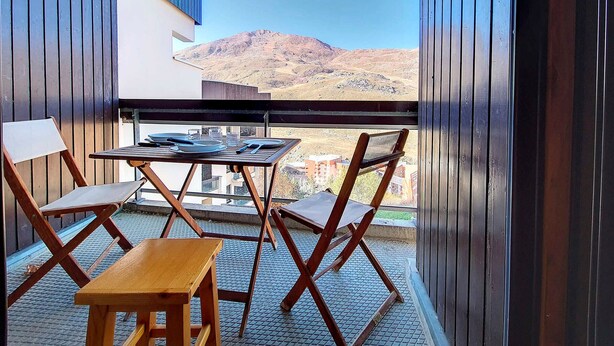 A balcony with a table and chairs, a view of mountains, and a wooden floor. - Spacious apartment for 6, steps from slopes, balcony with Masse view (Les Menuires)