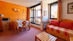 A cozy room with a wooden interior, a dining table with chairs, a sofa, and a window with curtains. - Spacious apartment for 6, steps from slopes, balcony with Masse view (Les Menuires)