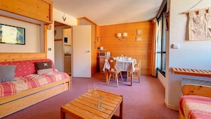 A cozy room with a wooden floor, a sofa, a dining table with chairs, and a TV. - Spacious apartment for 6, steps from slopes, balcony with Masse view (Les Menuires)