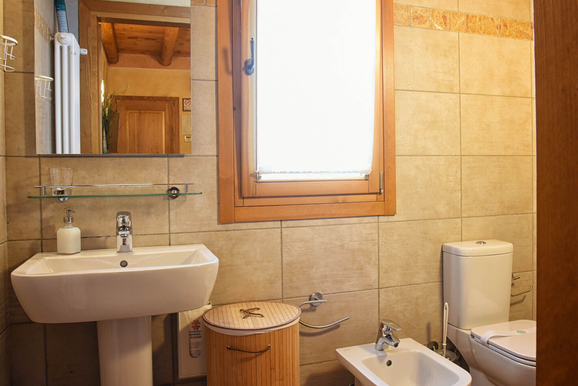Un bany amb una finestra gran, una banyera de fusta, un lavabo i un vàter.