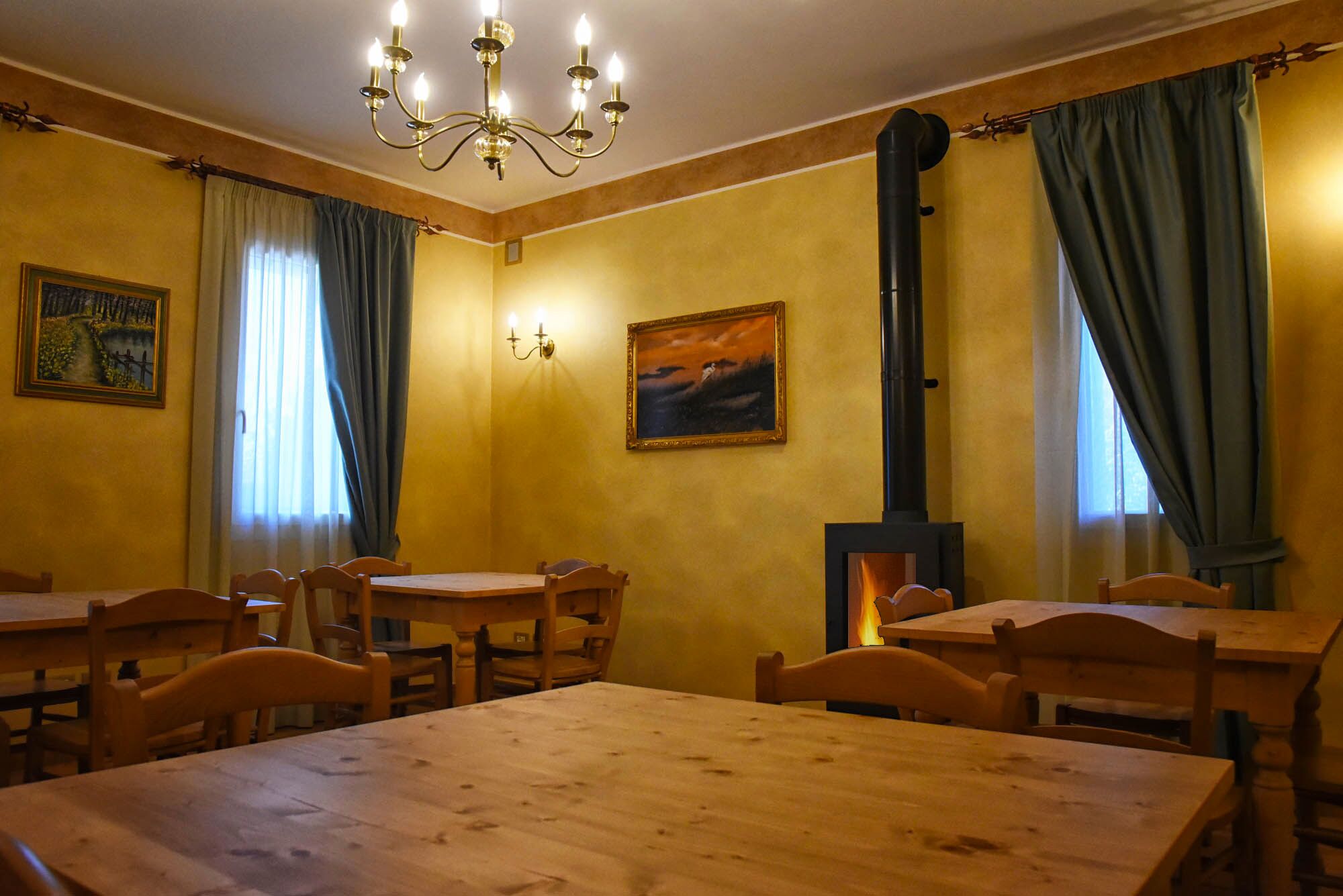 Un comedor con mesas y sillas de madera, una araña y una chimenea.