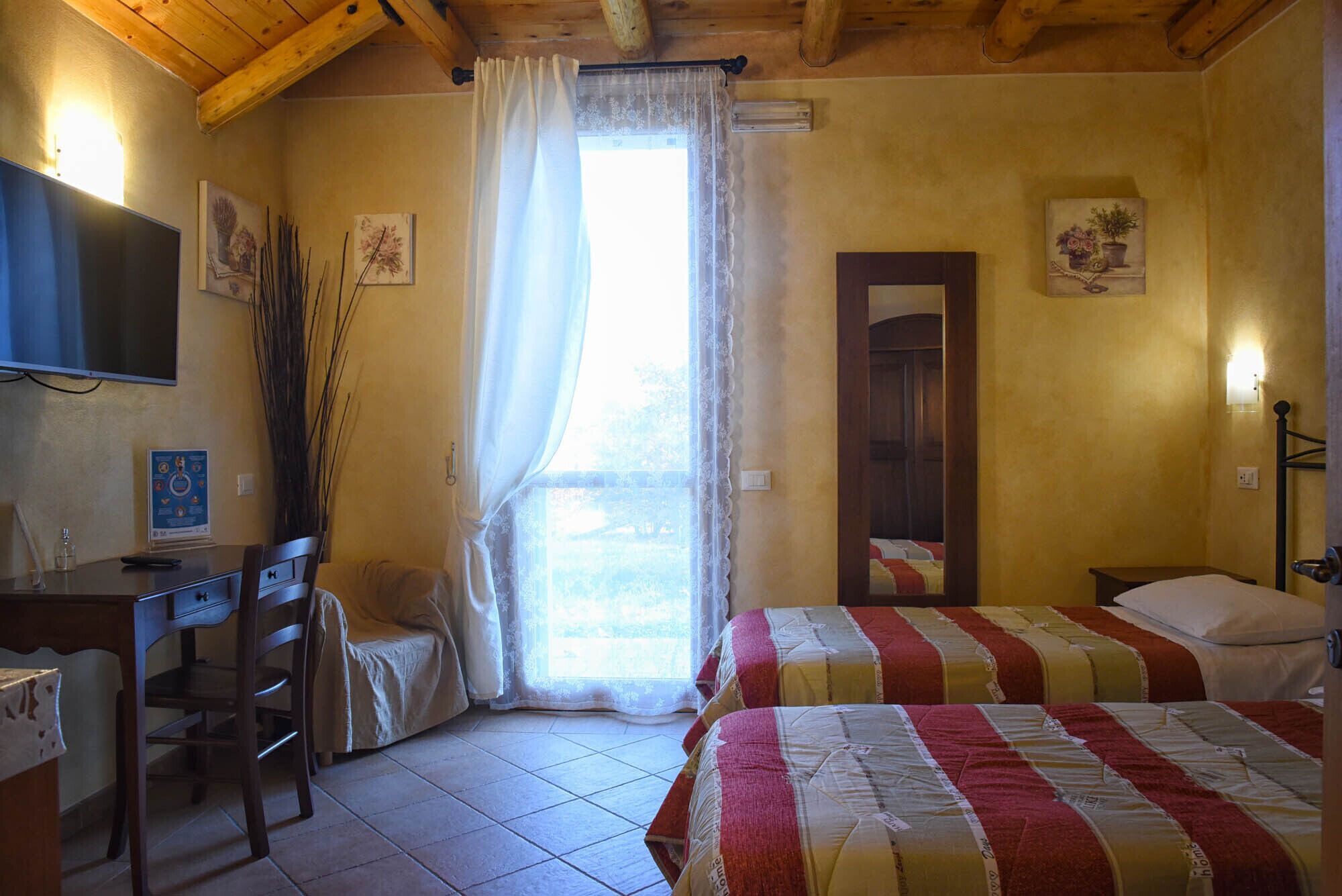 Una camera da letto con un letto, una scrivania, una sedia, una televisione e una finestra con tende.