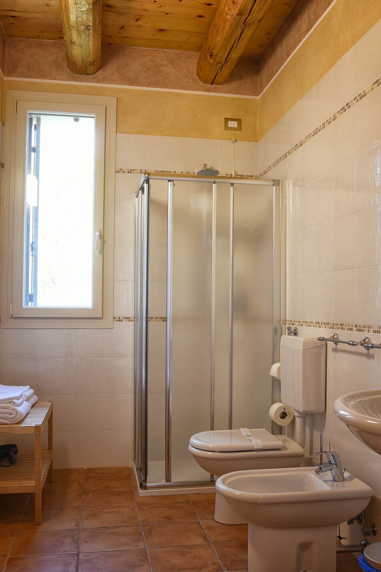 Un baño con cabina de ducha, inodoro, bidé y ventana que permite la entrada de luz natural.
