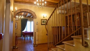 Eine Holztreppe führt zu einer oberen Etage, eine Kristallleuchter, ein Essbereich mit Tisch und Stühlen sowie eine rote Seilsperre.