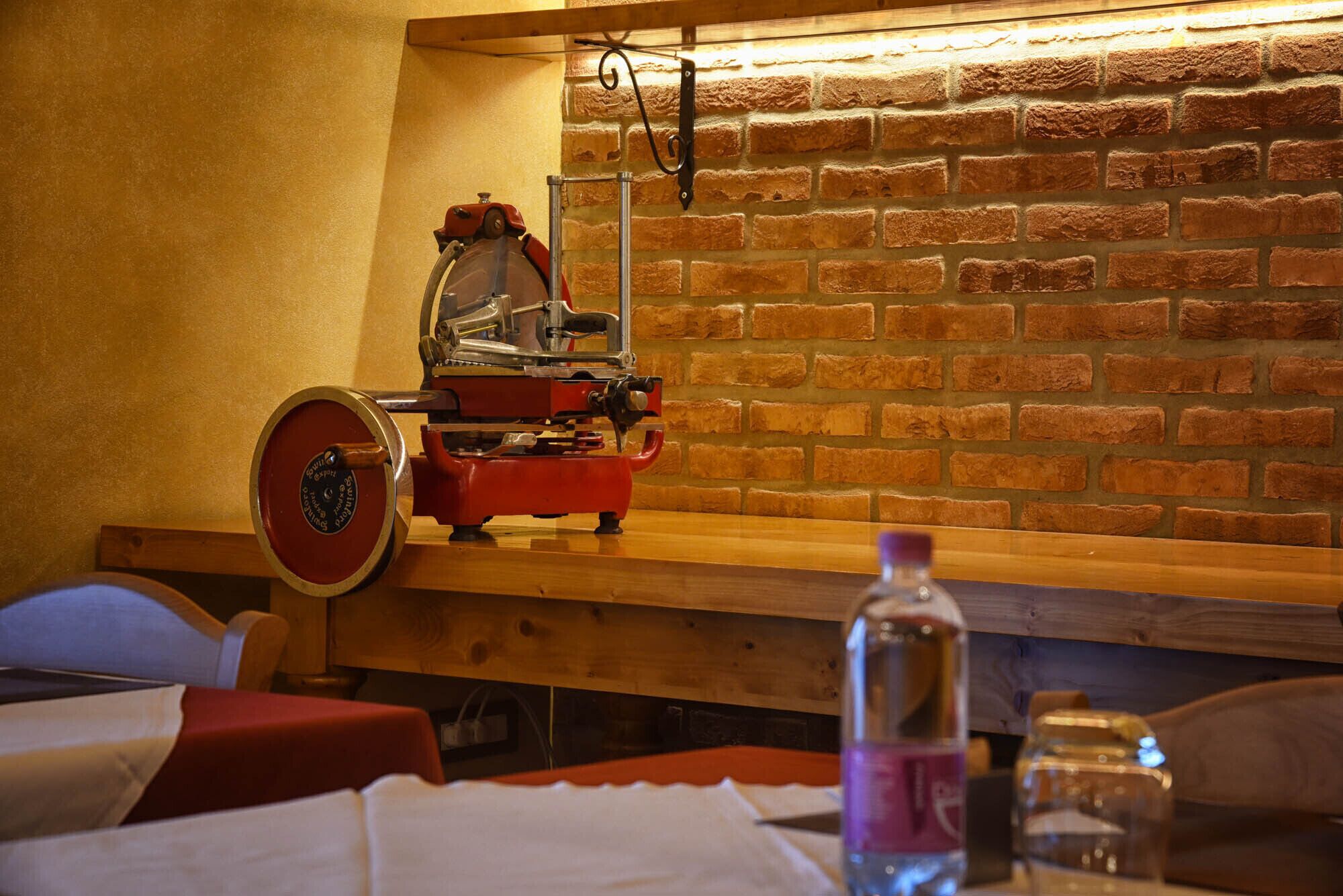 Una habitación con pared de ladrillo, banca de madera, máquina roja y una botella sobre una mesa.