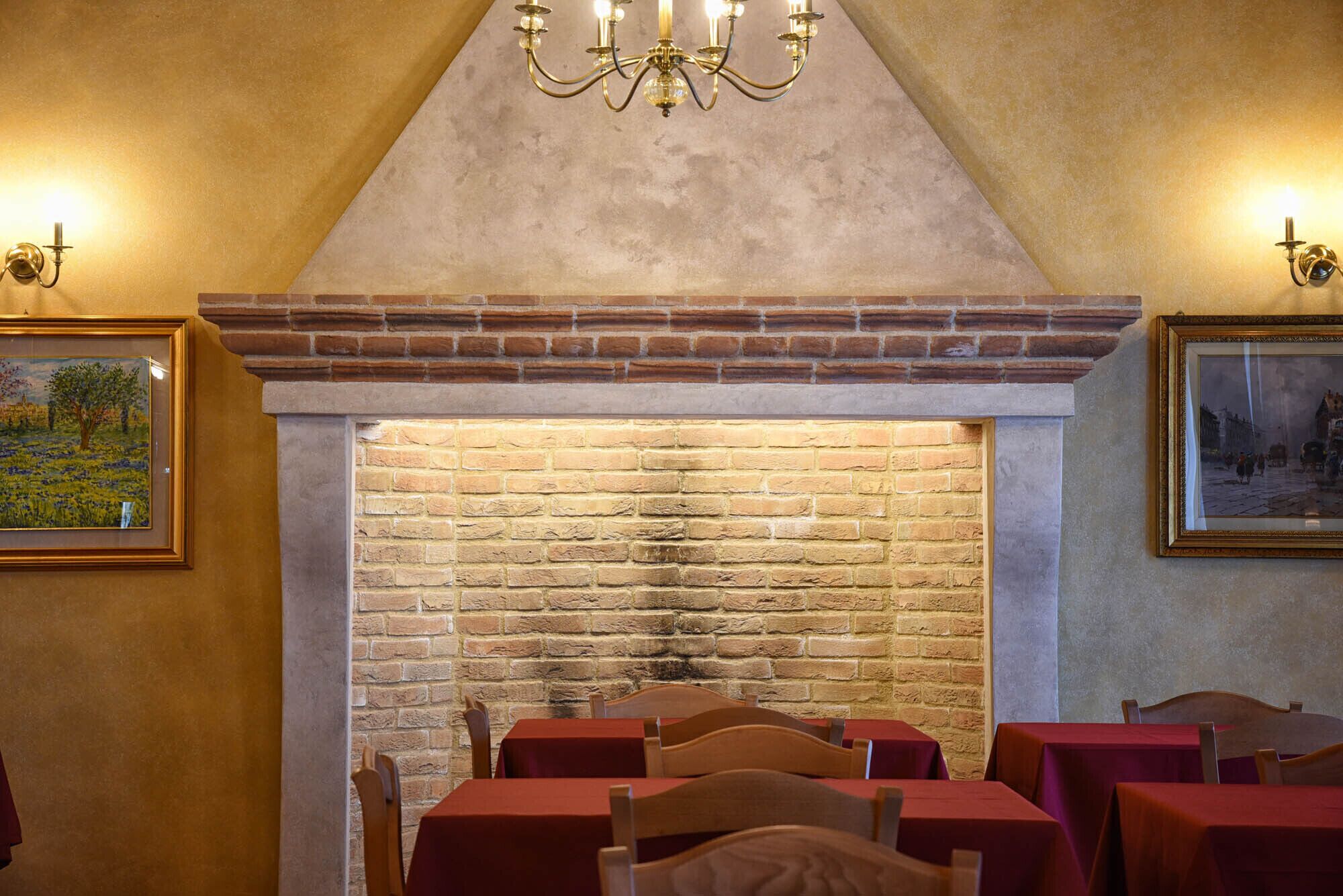 A dining area with brick walls, a fireplace, and tables with red tablecloths.