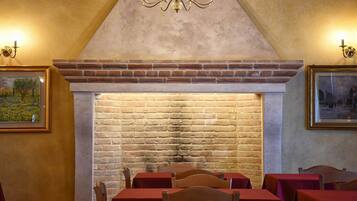 A dining area with brick walls, a fireplace, and tables with red tablecloths.