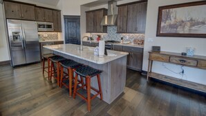 A modern kitchen with a central island, wooden cabinets, stainless steel appliances, and a herringbone tile backsplash. - River Run Townhomes 63 (Keystone)