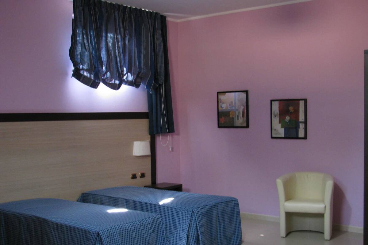 Habitación de hotel con una cama grande, dos mesitas de noche, una silla y dos cuadros en la pared.